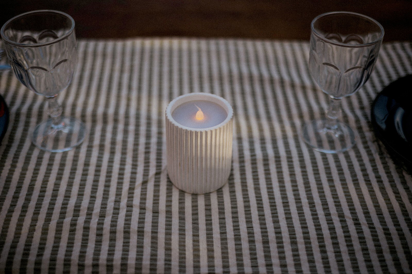 Outdoor-Kerze auf einem gestreiften Tischtuch, umgeben von zwei Weingläsern, aus der Vogelperspektive fotografiert.
