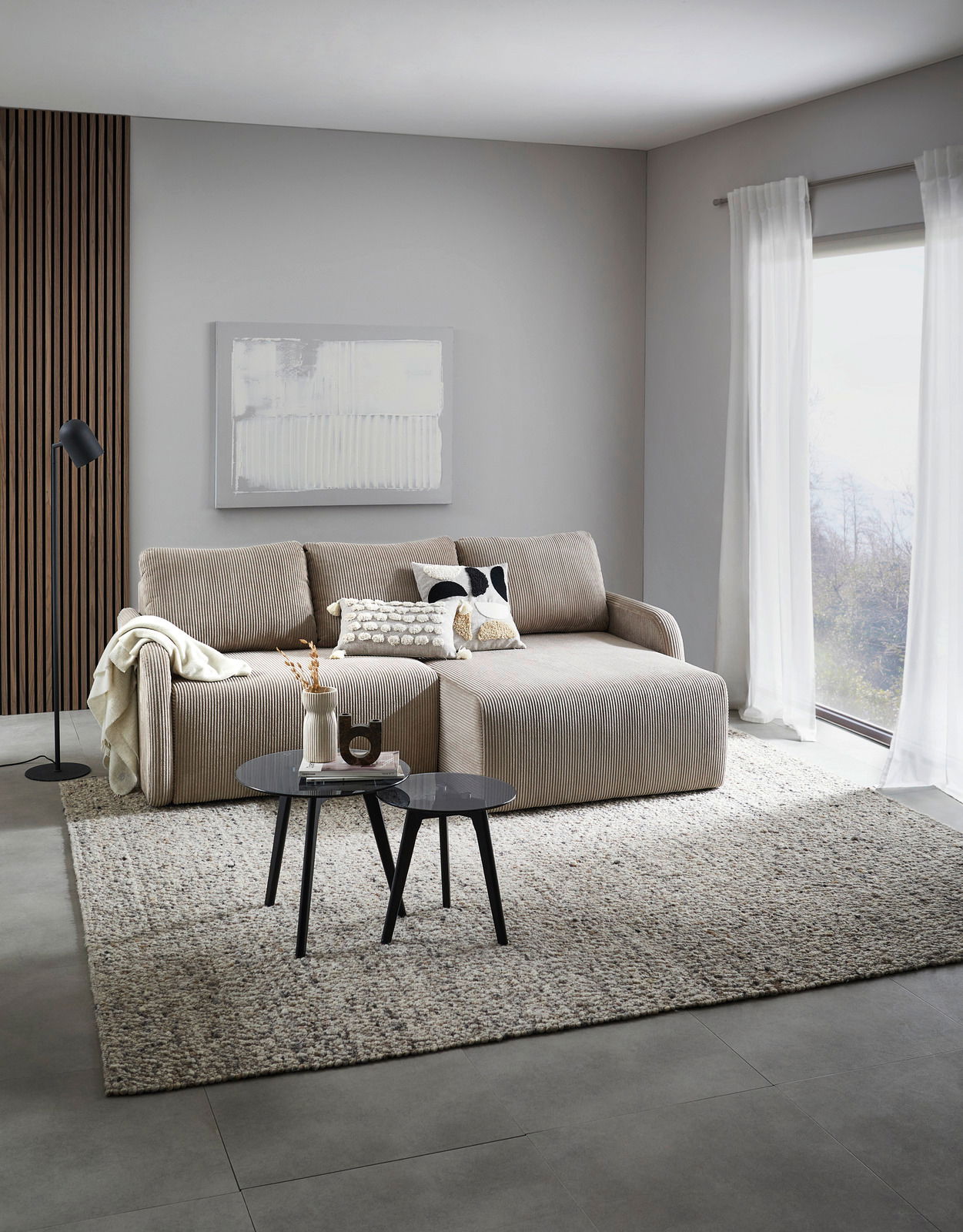 Ecksofa JENIFER in einem modernen Wohnzimmer, seitliche Perspektive, mit Kissen dekoriert, vor einem großen Fenster.