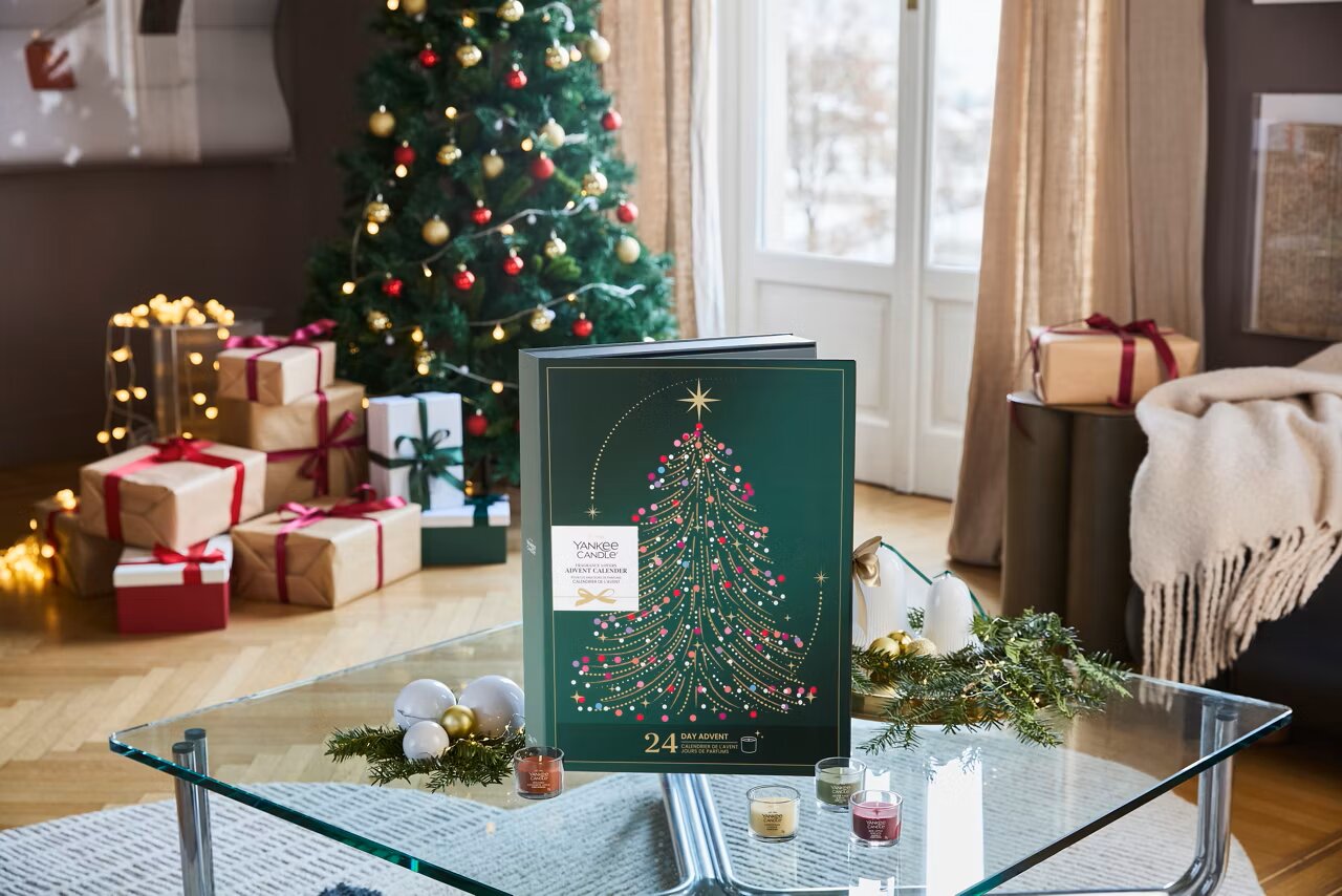 Yankee Candle Adventskalender in dunkelgrüner Geschenkbox mit stilisiertem Weihnachtsbaum, frontal auf einem Glastisch in festlich dekoriertem Wohnzimmer präsentiert
