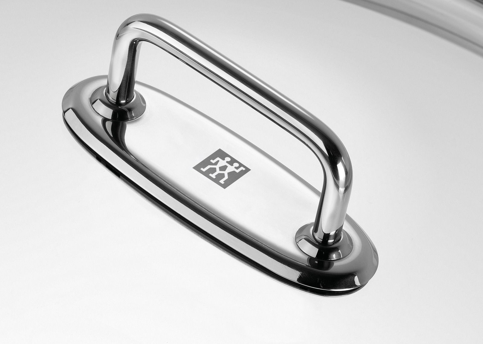 Nahaufnahme eines glänzenden Edelstahlgriffs auf einem Wok-Deckel, von oben betrachtet.