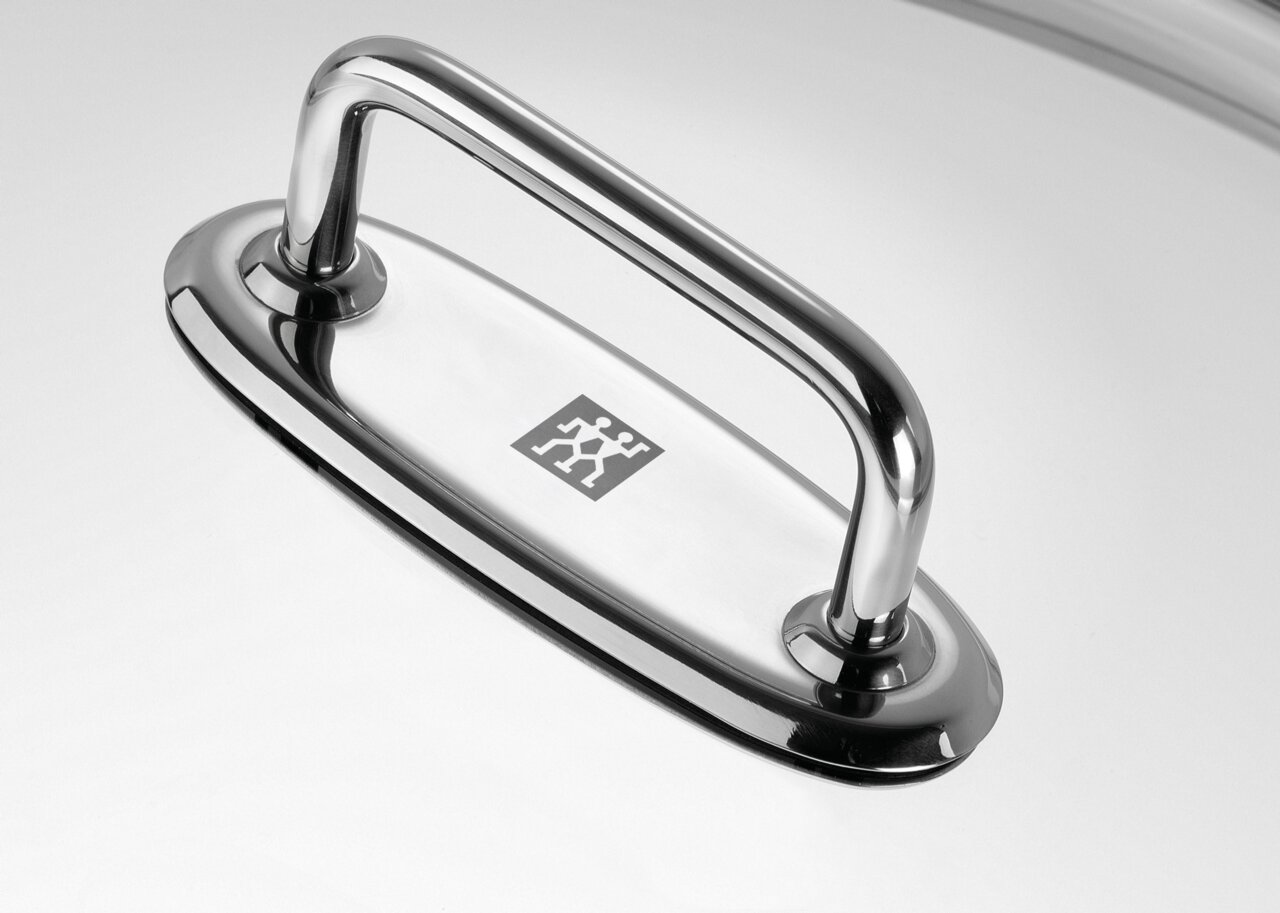 Nahaufnahme eines glänzenden Edelstahlgriffs auf einem Wok-Deckel, von oben betrachtet.