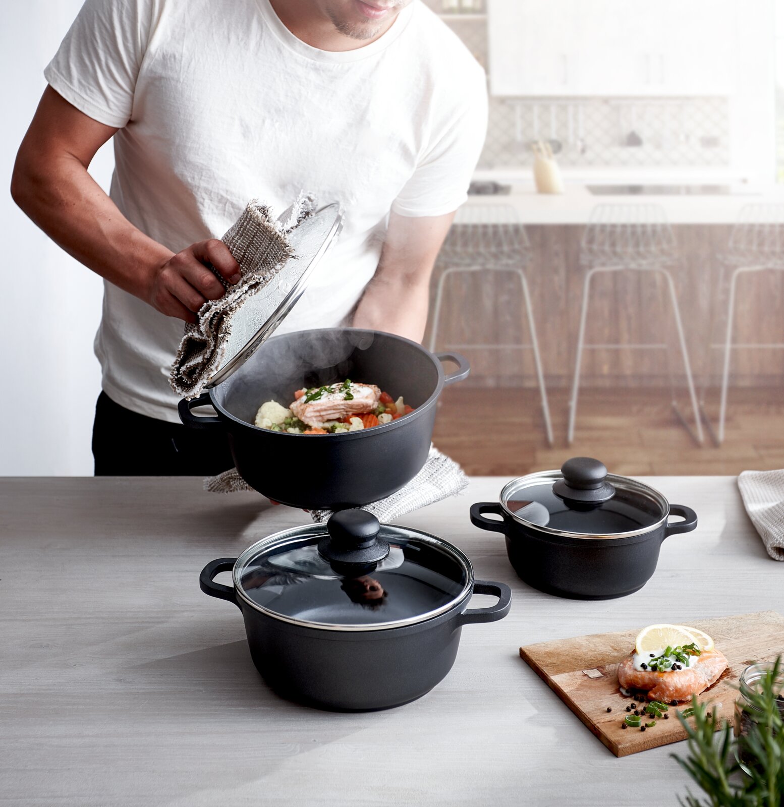 Driedelige pannenset in een moderne keuken, gezien van bovenaf, met een dampende pan en bereide zalm.