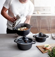 Driedelige pannenset in een moderne keuken, gezien van bovenaf, met een dampende pan en bereide zalm.