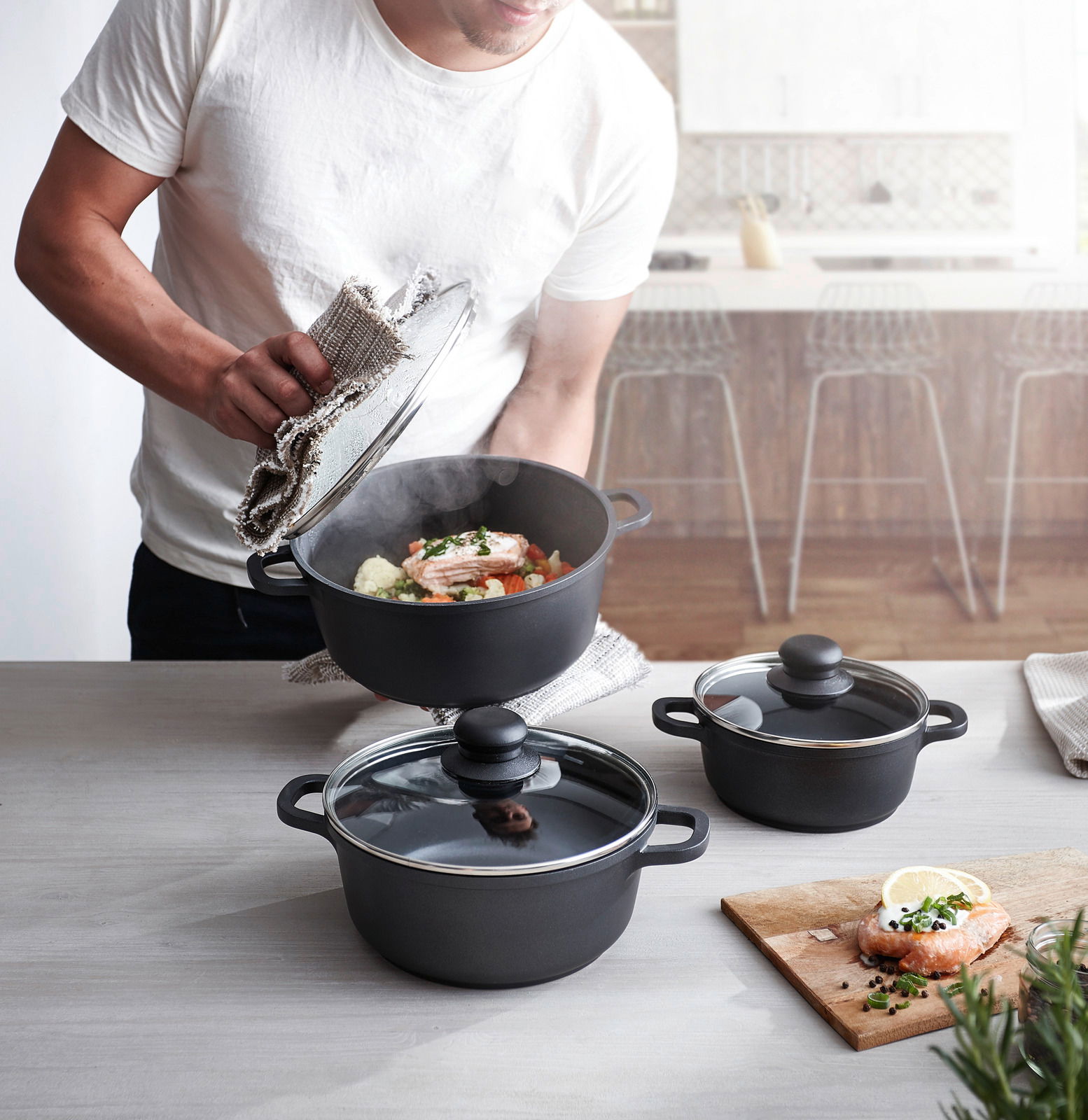 Dreiteiliges Topfset in moderner Küche, Perspektive von oben, mit dampfendem Topf und zubereitetem Lachs.