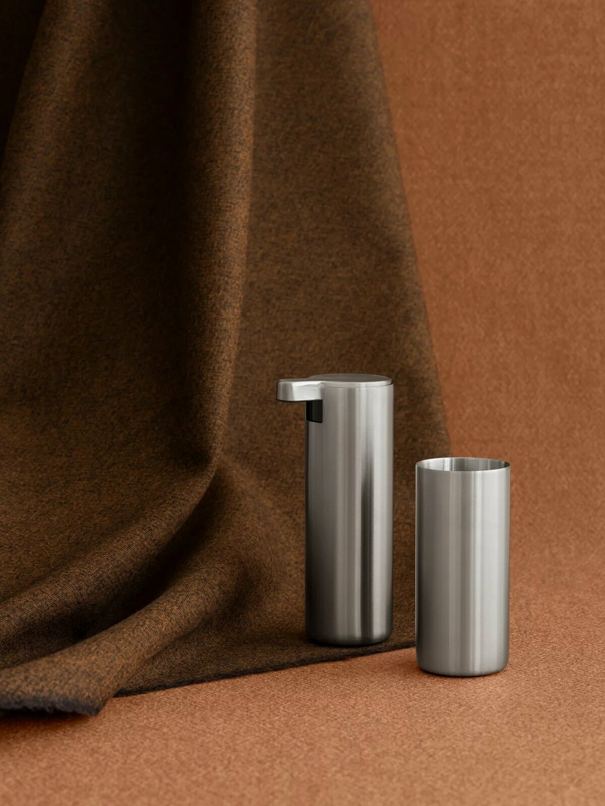 blomus Zahnputzbecher MODO Zwei Edelstahl-Zahnputzbecher auf braunem Stoffhintergrund, seitliche Perspektive.