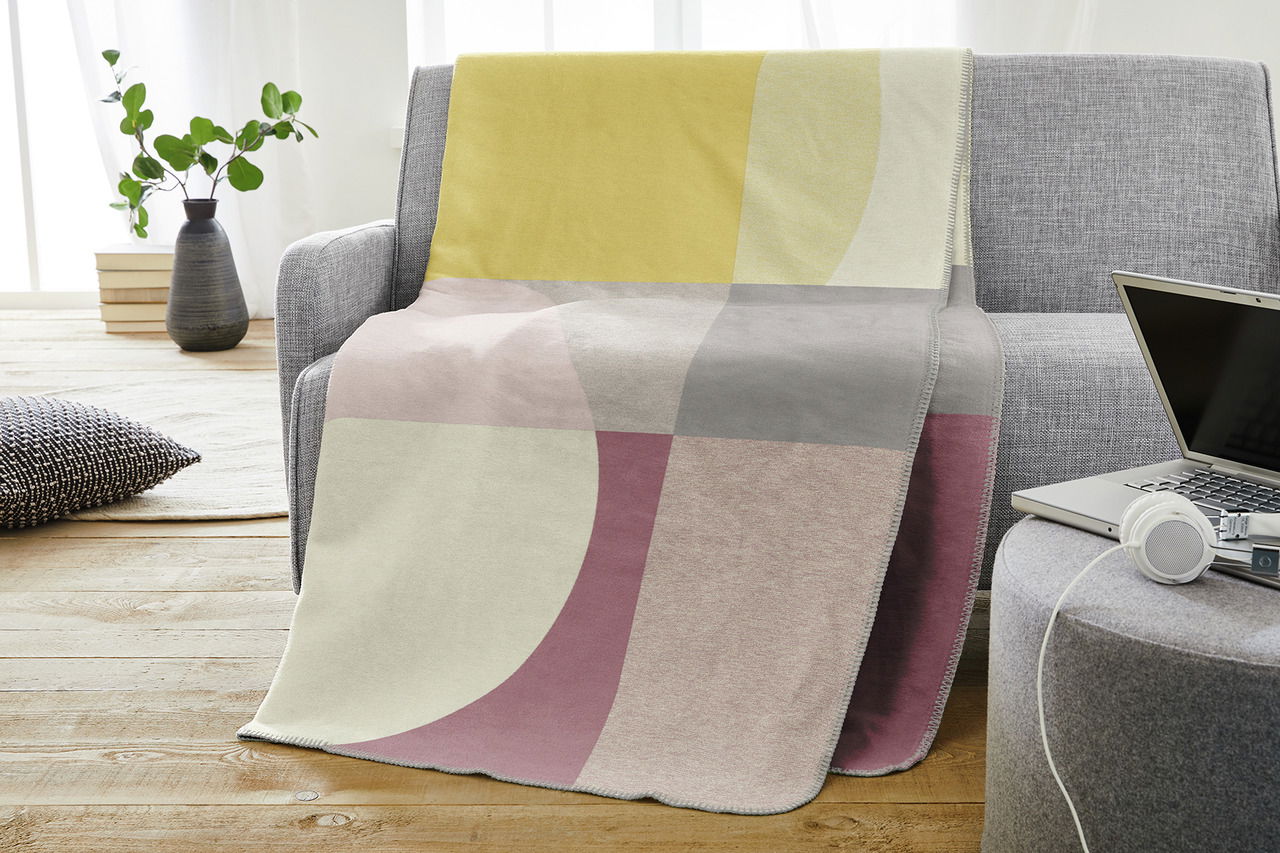 Jacquard Decke mit geometrischem Muster in Pastellfarben auf einem grauen Sofa, seitliche Perspektive