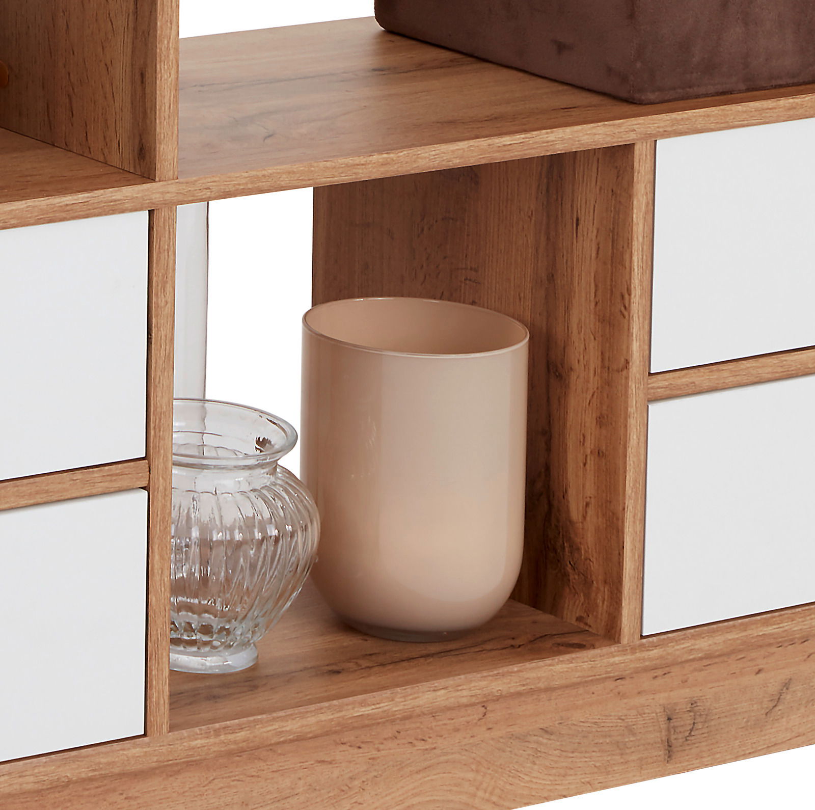 Nahaufnahme eines Raumteilers oder Regals aus Holz mit weißen Schubladenfronten, dekoriert mit einem Glasgefäß und einem beigen Behälter.