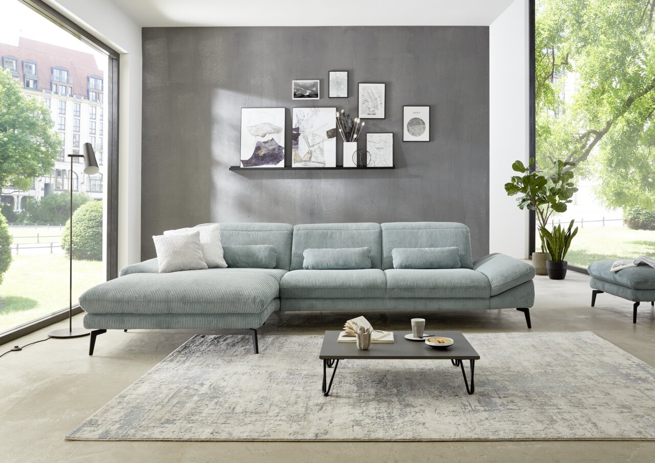 Beldomo System Longchair-combinatie AUGSBURG Moderne longchair-combinatie in een lichte woonkamer met grote ramen, een grijze muur en decoratieve schilderijen. Aanzicht van voren.