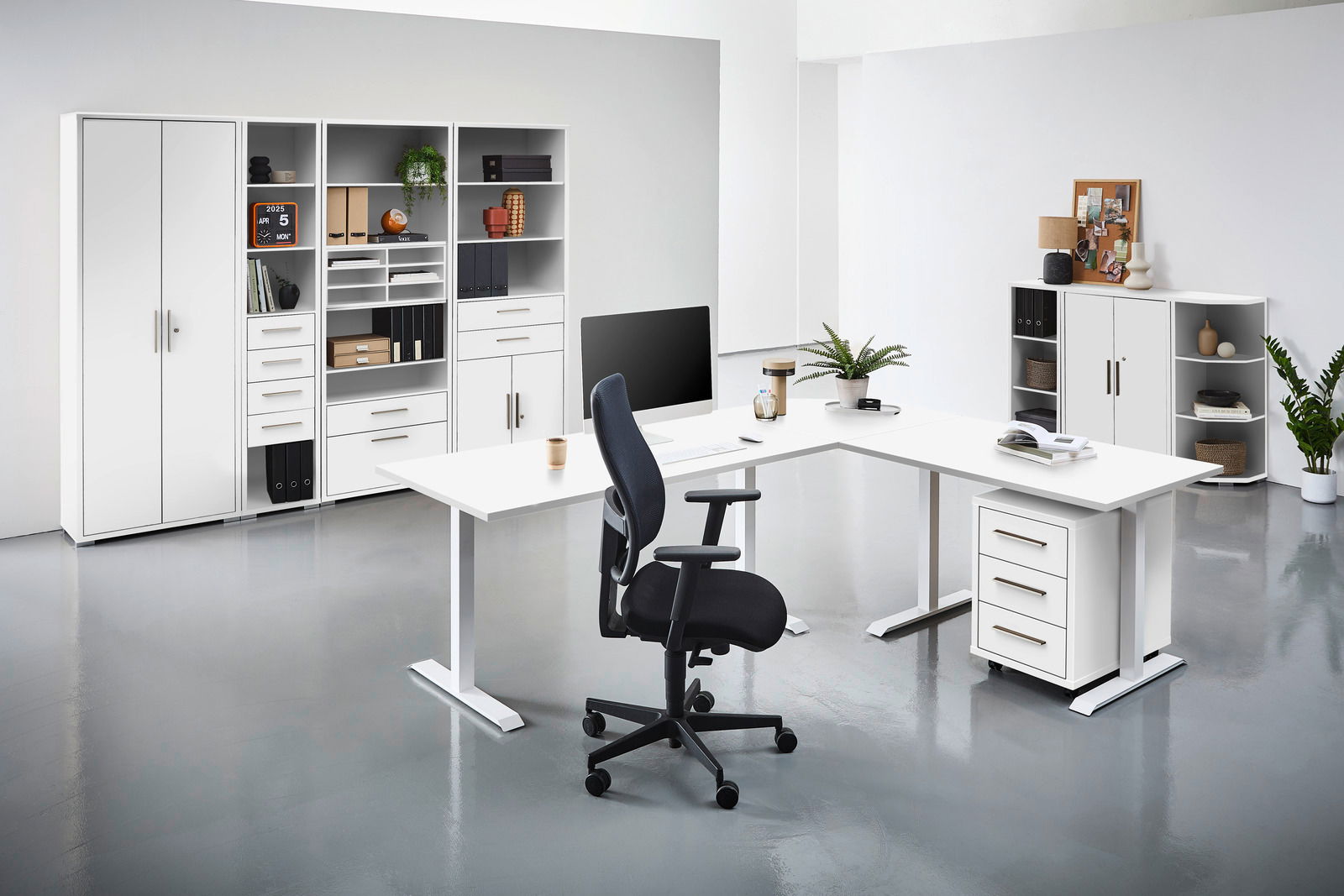 Moderne Büroumgebung mit weißen Schreibtischen, Regalen und einem ergonomischen Bürostuhl, aus der Perspektive von vorne betrachtet.