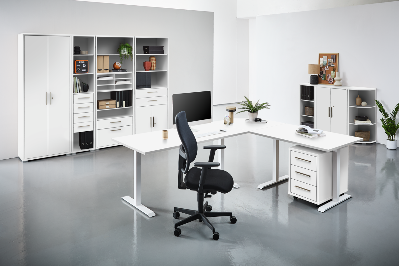 Moderne Büroumgebung mit weißen Schreibtischen, Regalen und einem ergonomischen Bürostuhl, aus der Perspektive von vorne betrachtet.