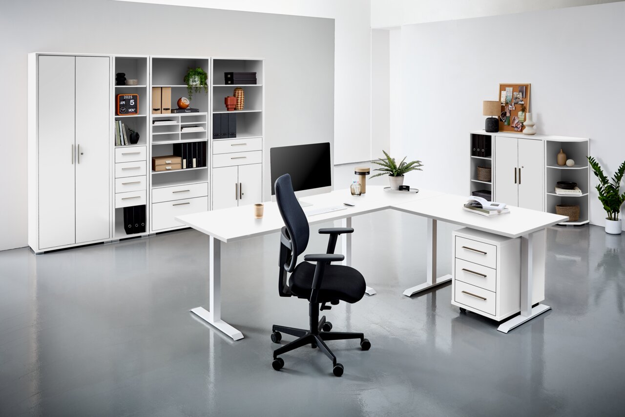Moderne Büroumgebung mit weißen Schreibtischen, Regalen und einem ergonomischen Bürostuhl, aus der Perspektive von vorne betrachtet.
