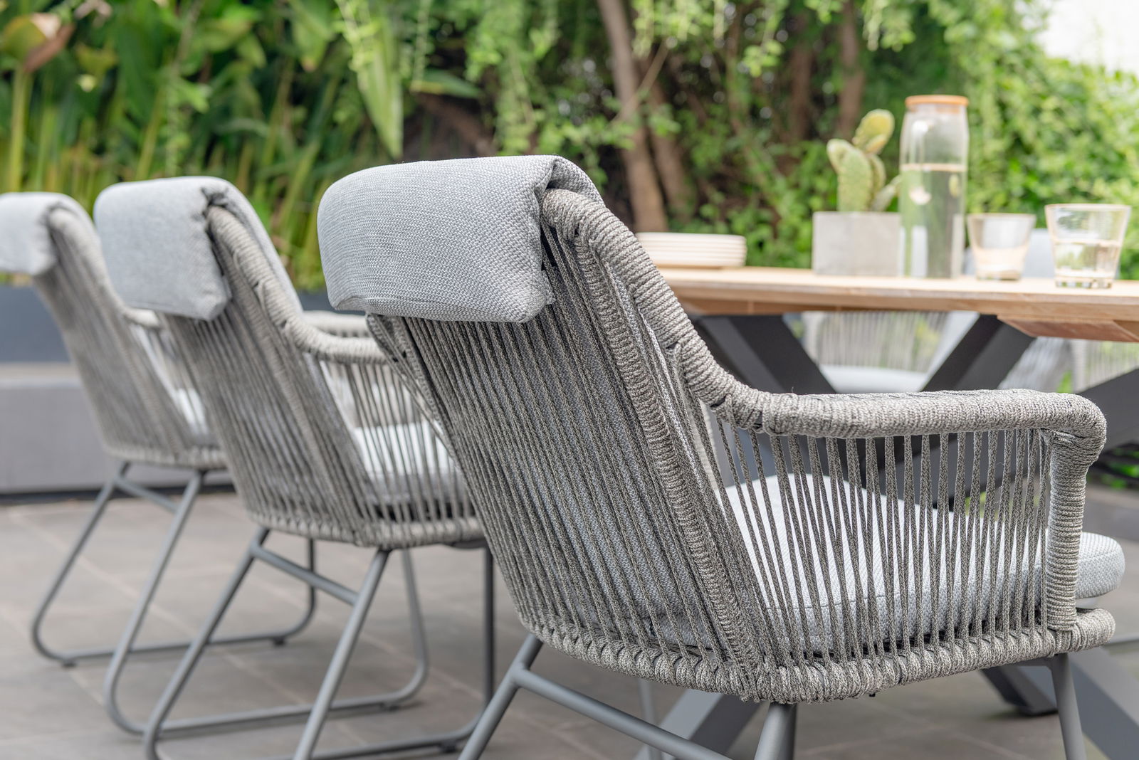 Rückansicht von grauen Armlehnstühlen mit geflochtenem Design, die um einen Holztisch im Freien angeordnet sind.