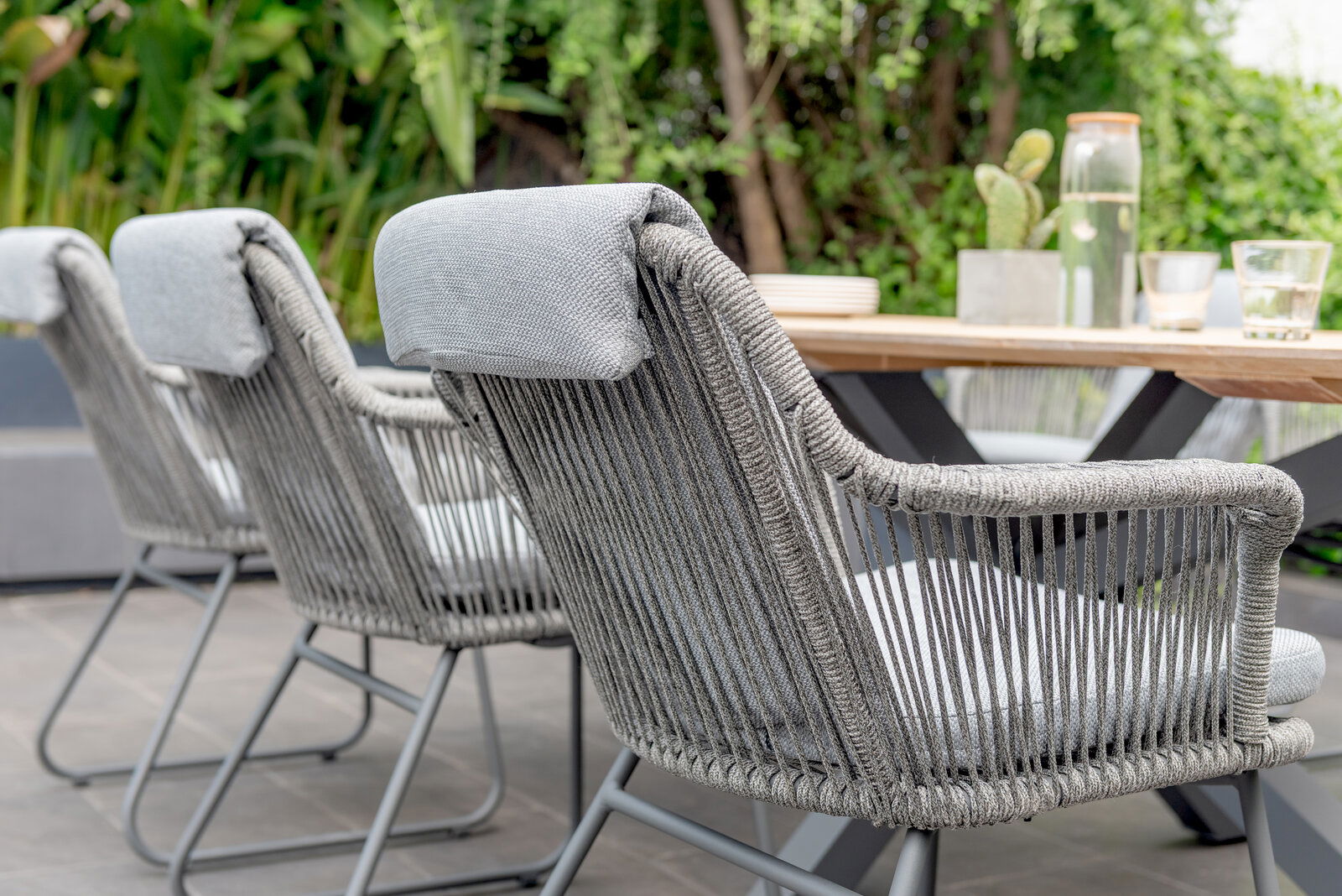 Rückansicht von grauen Armlehnstühlen mit geflochtenem Design, die um einen Holztisch im Freien angeordnet sind.