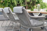 Rückansicht von grauen Armlehnstühlen mit geflochtenem Design, die um einen Holztisch im Freien angeordnet sind.