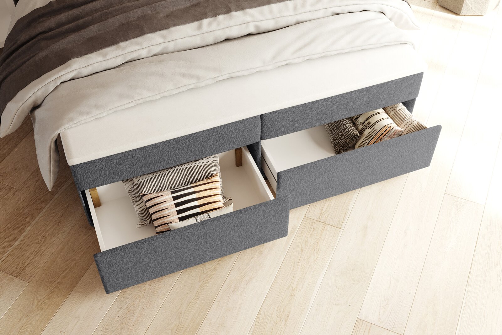 Graues Polsterbett/Boxspringbett mit zwei herausgezogenen Schubladen unter dem Bett, darin Kissen verstaut, Ansicht schräg von oben