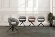 Vier moderne fauteuils in verschillende kleuren, gezien vanaf de voorkant in een elegante ruimte met lambrisering en planten.