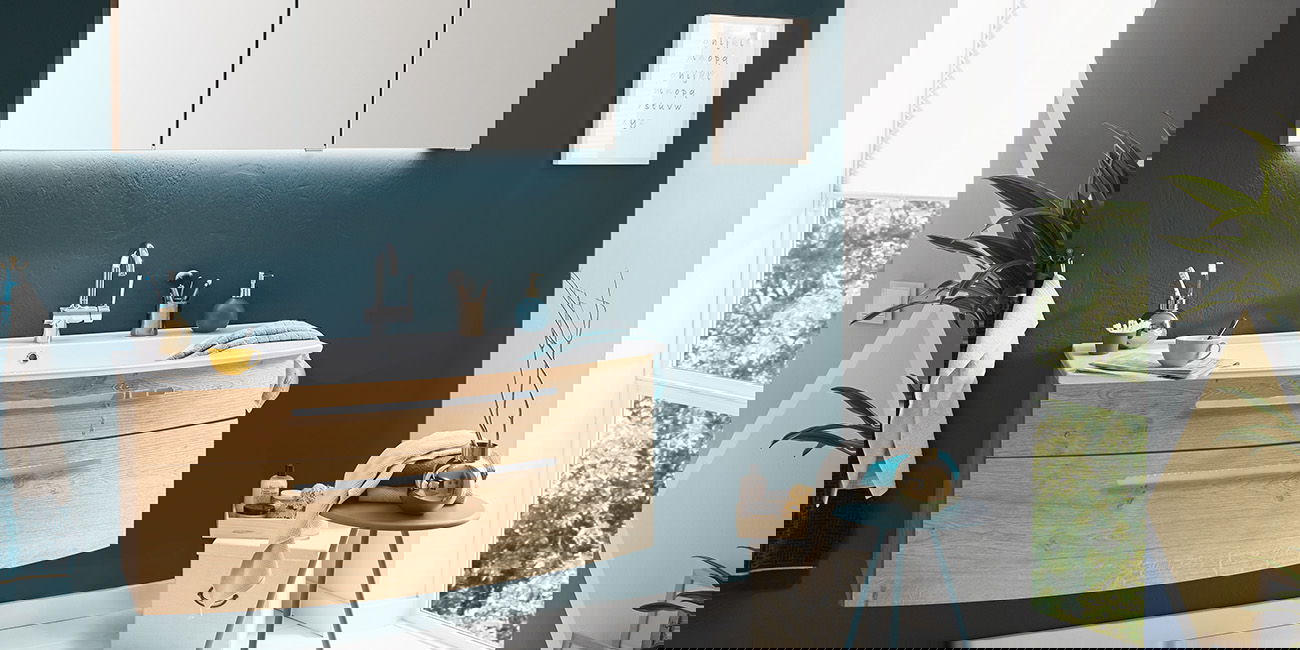 Modernes Bad mit Holz-Waschbecken, blaugrüner Wand und großem Fenster mit Licht.