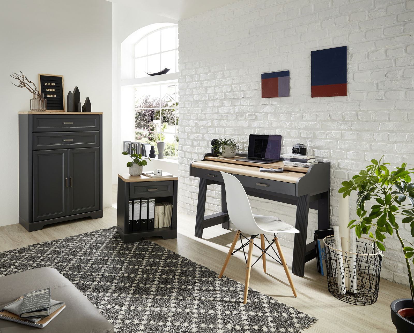 Moderne Büromöbel in einem hellen Raum, bestehend aus einem grauen Aktenschrank, einem Rollcontainer und einem Schreibtisch mit Dekorationen, aus der Perspektive von vorne betrachtet.