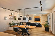 Moderne Wohnzimmerszene mit Schienenspot Tubo an der Decke, Blick von der Seite auf den Essbereich mit Holztisch und schwarzen Stühlen.