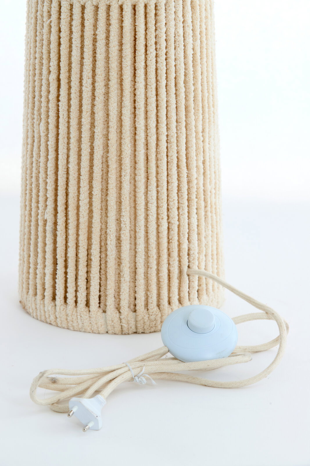 Nahaufnahme einer Stehleuchte mit strukturiertem, beigem Lampenschirm und einem weißen Fußschalter mit Kabel.