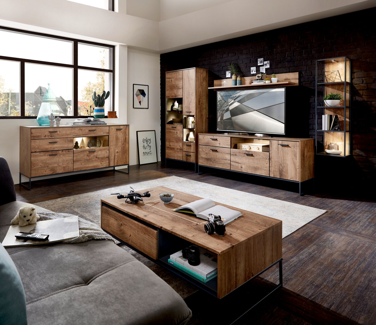 Wohnzimmeransicht mit moderner Holzmöbelkombination, bestehend aus Sideboard, Vitrine und TV-Unterteil, in einem hellen Raum mit großen Fenstern.