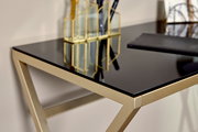Nahaufnahme eines eleganten Schreibtisches mit schwarzer Glasplatte und goldfarbenem Metallrahmen, seitliche Perspektive.