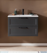 Frontale Ansicht eines modernen Waschtisch-Sets mit zwei Schubladen in dunklem Grau, weißer Waschbeckenoberfläche und stilvollen schwarzen Griffen, dekoriert mit Seifenspender und Accessoires.