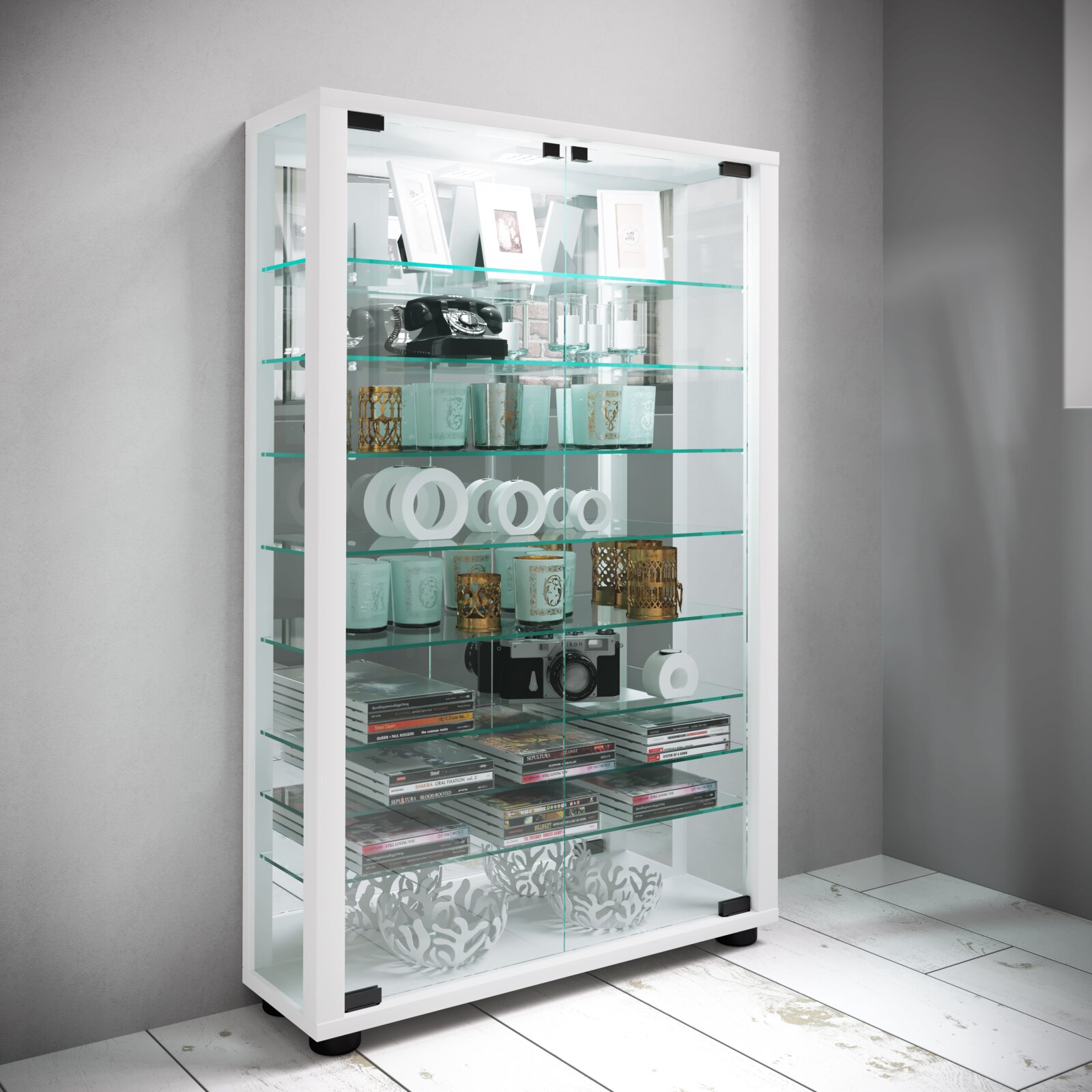 VCM Standvitrine LUMO Weiße Glasvitrine mit Glastüren und mehreren Glasböden, gefüllt mit Dekoartikeln und Büchern, in schräger Frontansicht vor grauer Wand