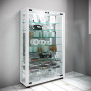 Weiße Glasvitrine mit Glastüren und mehreren Glasböden, gefüllt mit Dekoartikeln und Büchern, in schräger Frontansicht vor grauer Wand