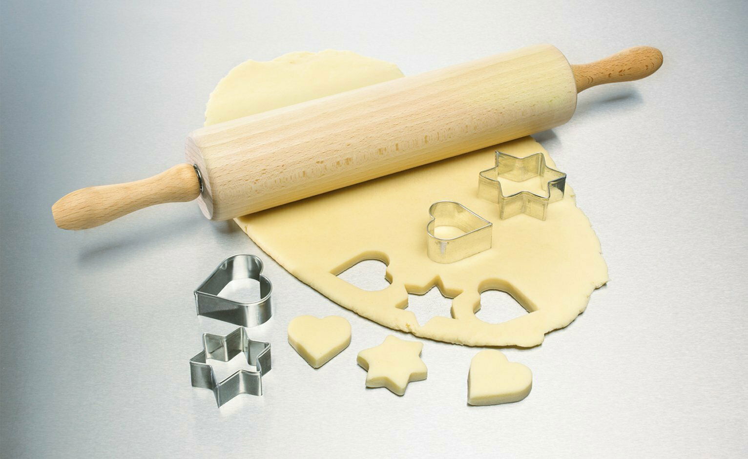 Holzteigroller auf ausgerolltem Teig mit Ausstechformen in Herz- und Sternform, seitliche Perspektive
