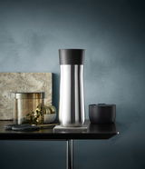 Eleganter Impulse Isolierbecher 0,35l in Edelstahloptik mit schwarzem Deckel, seitliche Perspektive auf einem Tisch arrangiert.