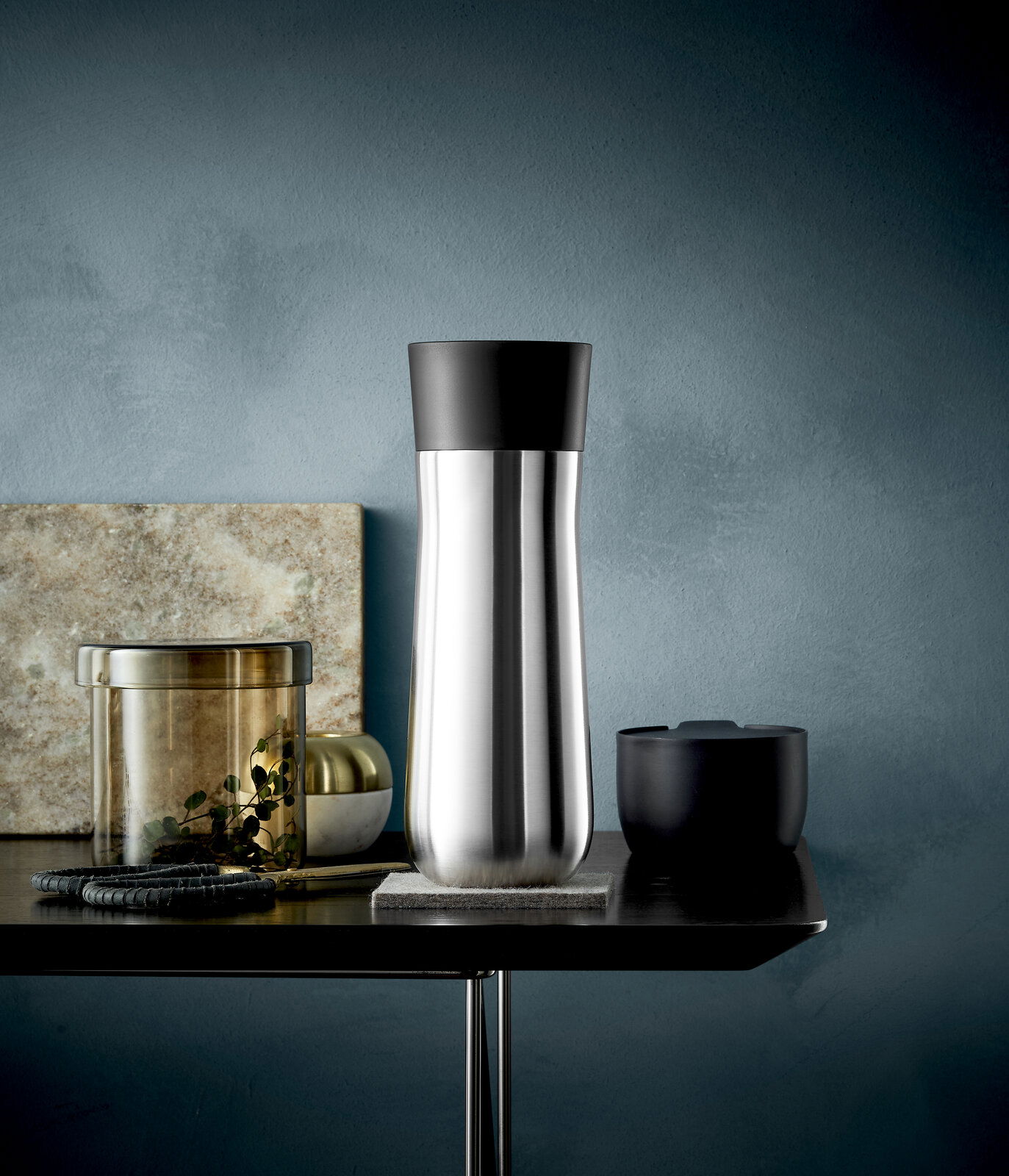 Eleganter Impulse Isolierbecher 0,35l in Edelstahloptik mit schwarzem Deckel, seitliche Perspektive auf einem Tisch arrangiert.