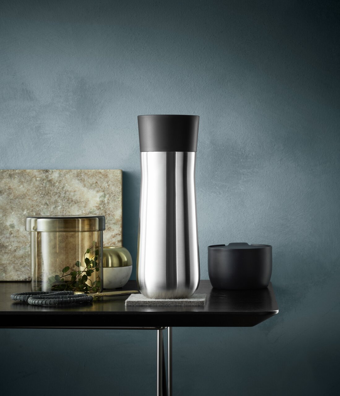 Eleganter Impulse Isolierbecher 0,35l in Edelstahloptik mit schwarzem Deckel, seitliche Perspektive auf einem Tisch arrangiert.