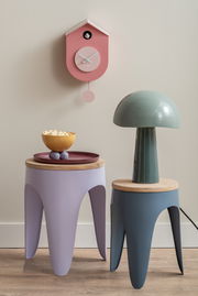 Rosa Wanduhr in Vogelhausform mit Pendel, frontal an der Wand montiert, neben modernen Beistelltischen und einer Lampe.