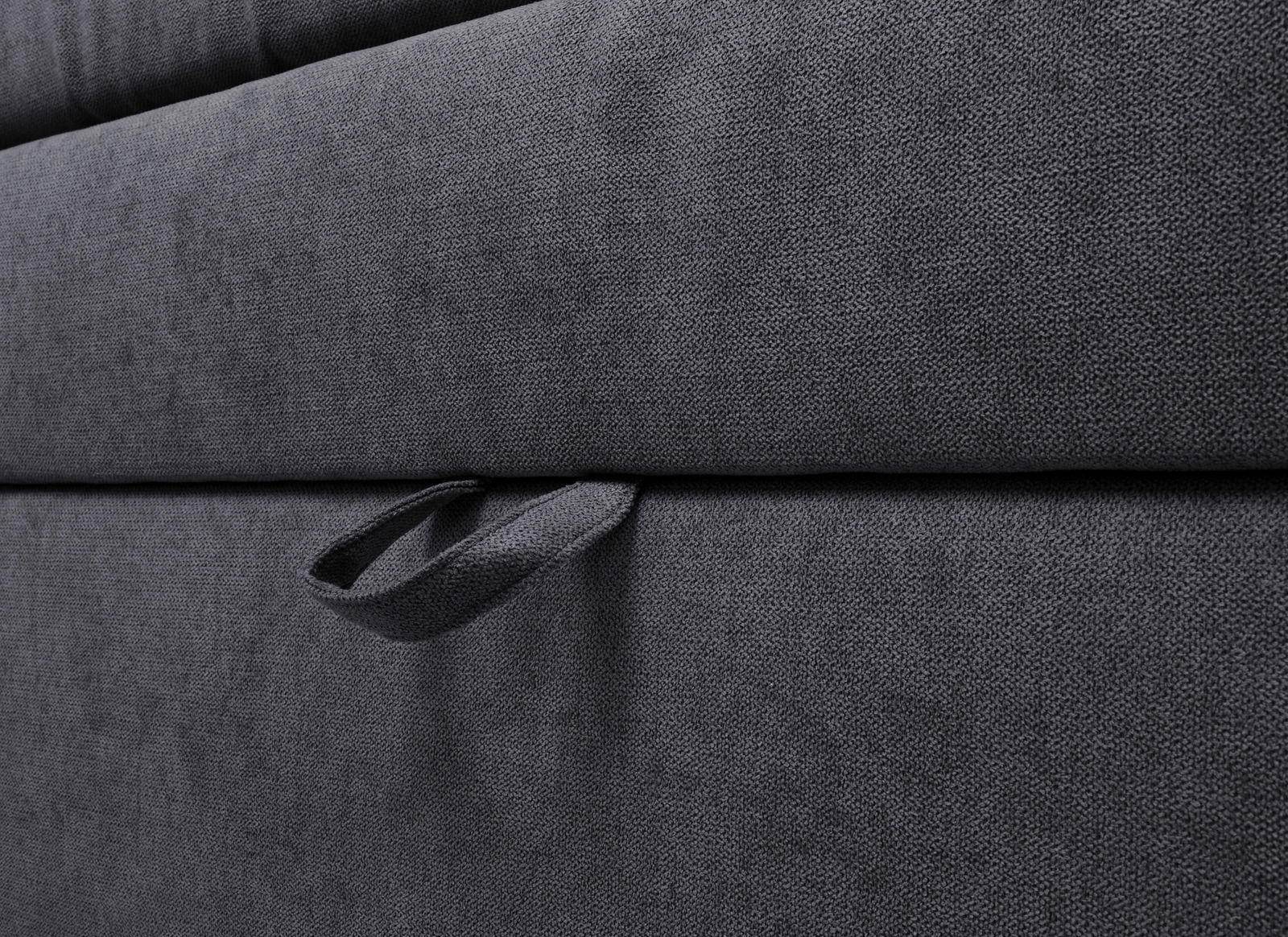 Nahaufnahme eines grauen Boxspringbetts mit Stoffbezug und Griff, seitliche Perspektive