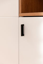 Nahaufnahme eines Highboards mit weißer Tür und schwarzem Griff, obere Ecke zeigt Holzdetail.