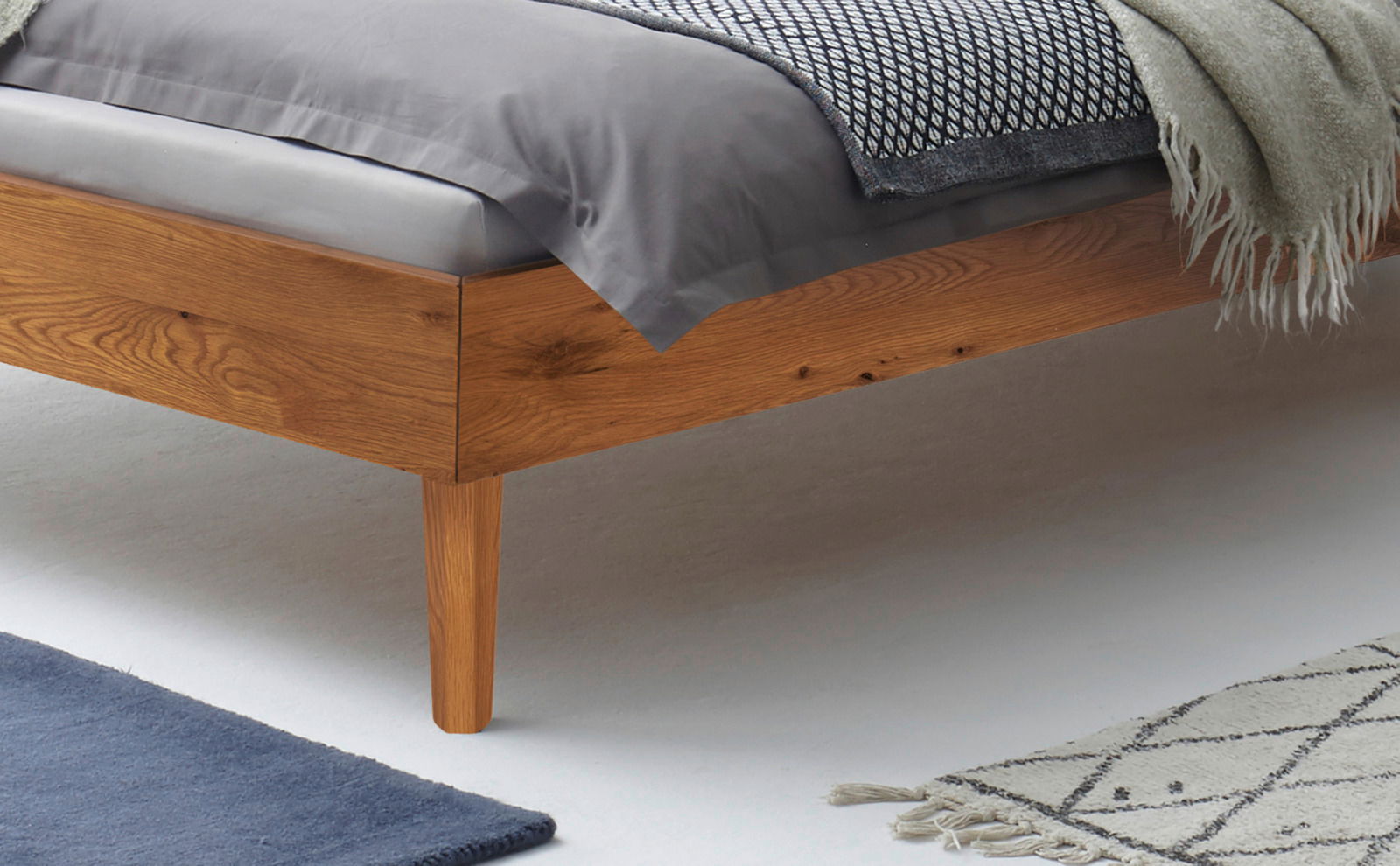 Nahaufnahme eines Bettgestells aus Holz mit Bettwäsche in einem modernen Schlafzimmer, seitliche Perspektive