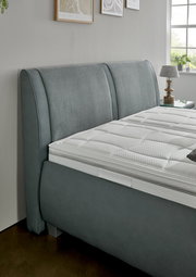 Graues Polsterbett mit elegantem Kopfteil, seitliche Perspektive