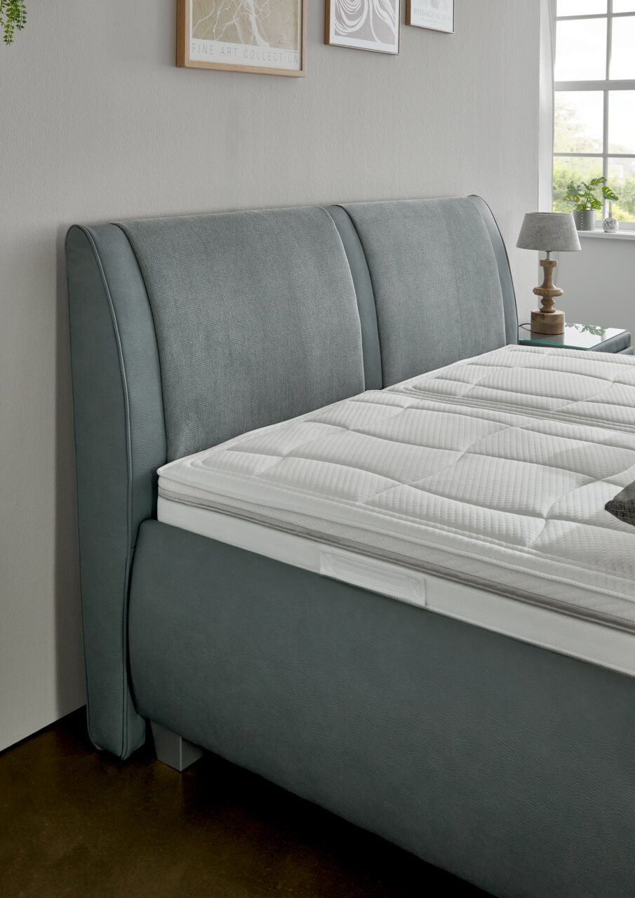 Graues Polsterbett mit elegantem Kopfteil, seitliche Perspektive