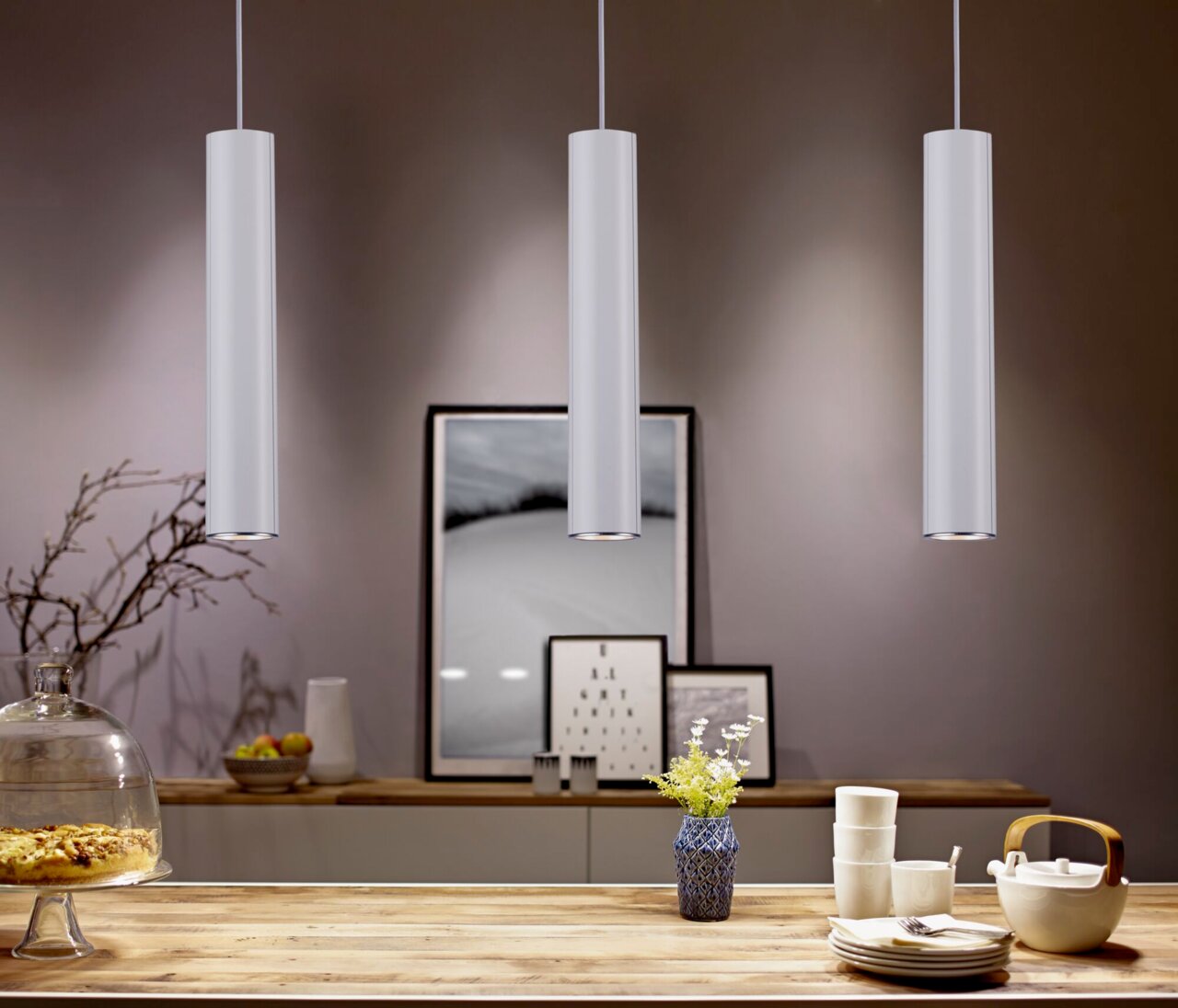 Drie moderne, cilindervormige hanglampen in een stijlvol ingerichte ruimte, gezien vanuit het perspectief van een eettafel.