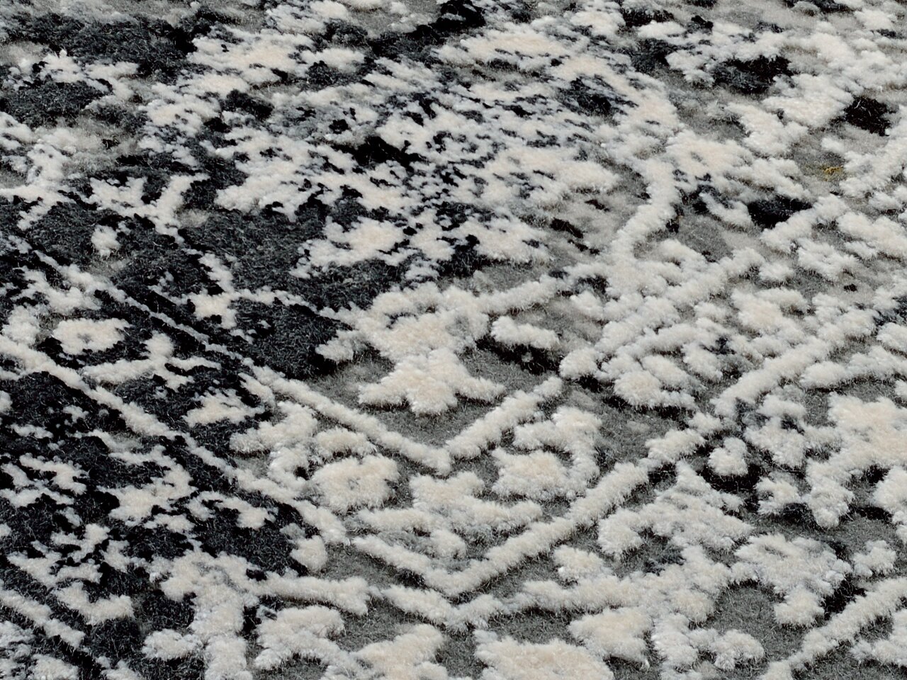 Nahaufnahme eines Designer-Teppichs mit einem schwarz-weißen, abstrakten Muster. Die Perspektive zeigt eine diagonale Ansicht der Textur.