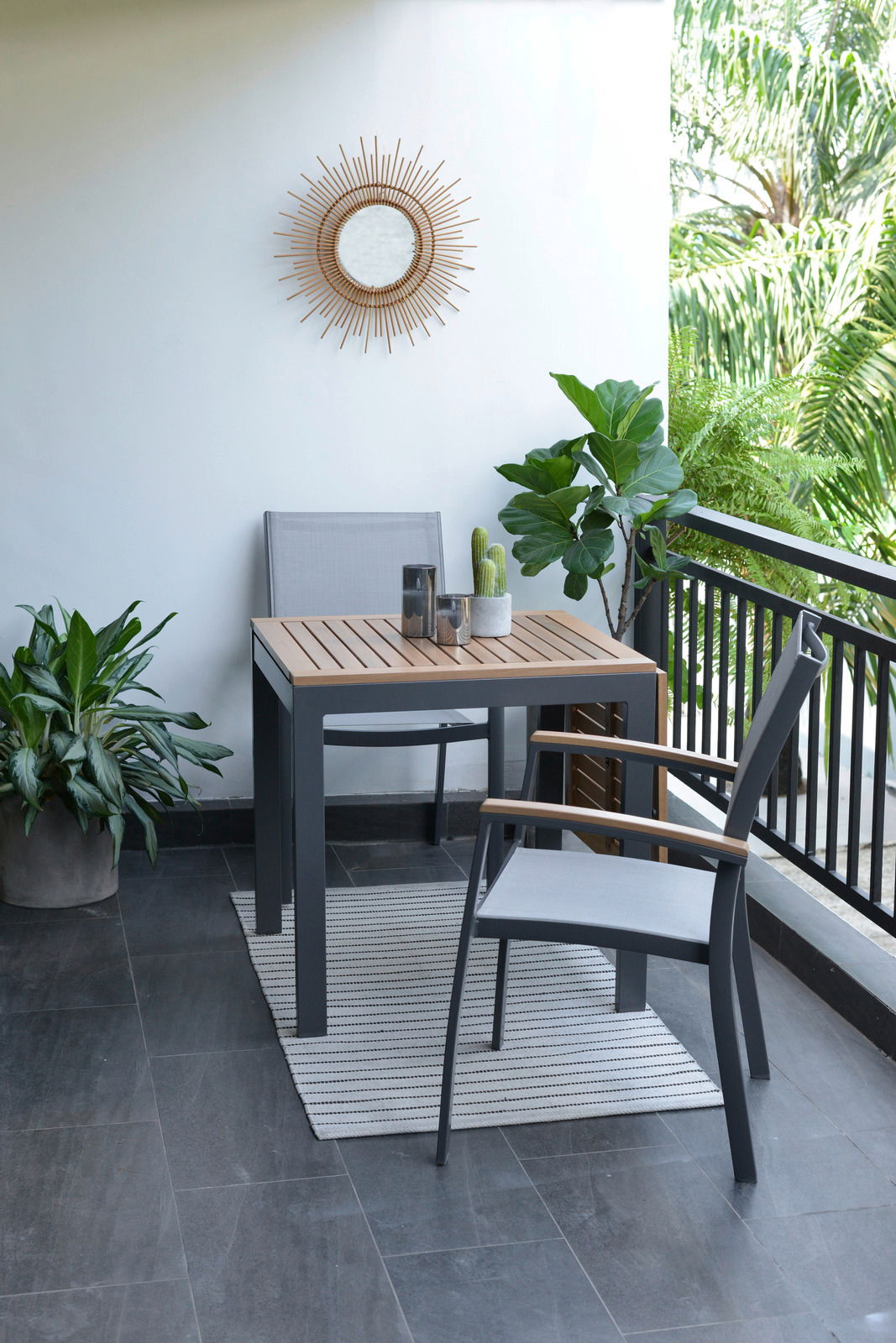 Moderner Gartentisch mit zwei Stühlen auf einem Balkon, umgeben von Pflanzen, aus der Seitenperspektive fotografiert.