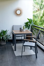 Moderner Gartentisch mit zwei Stühlen auf einem Balkon, umgeben von Pflanzen, aus der Seitenperspektive fotografiert.