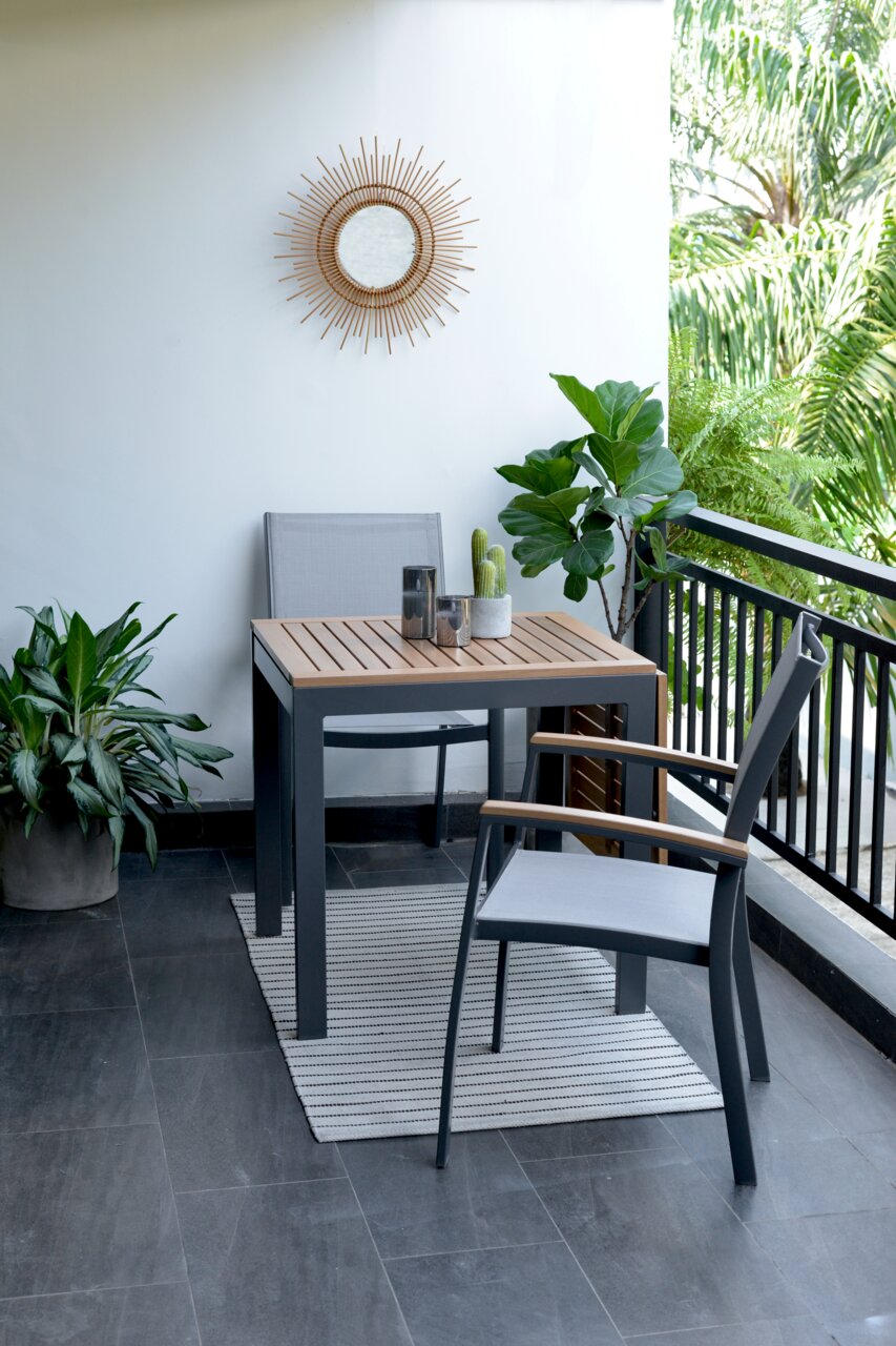 Een moderne tuintafel met twee stoelen op een balkon, omringd door planten, gefotografeerd vanuit een zijaanzicht.