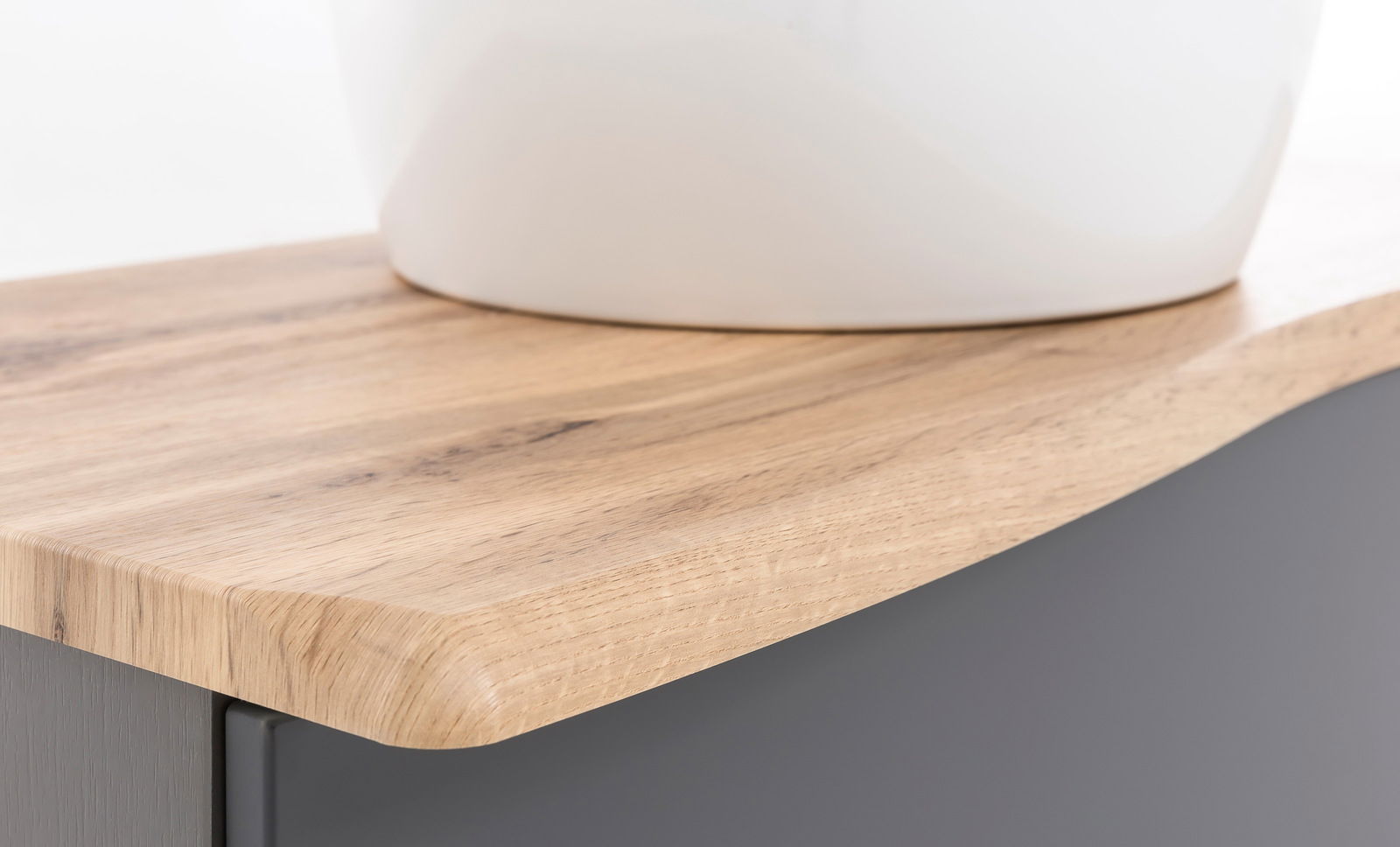 Nahaufnahme eines Waschtisch-Sets mit einer eleganten Holzoberfläche und einem weißen Waschbecken, seitliche Perspektive.