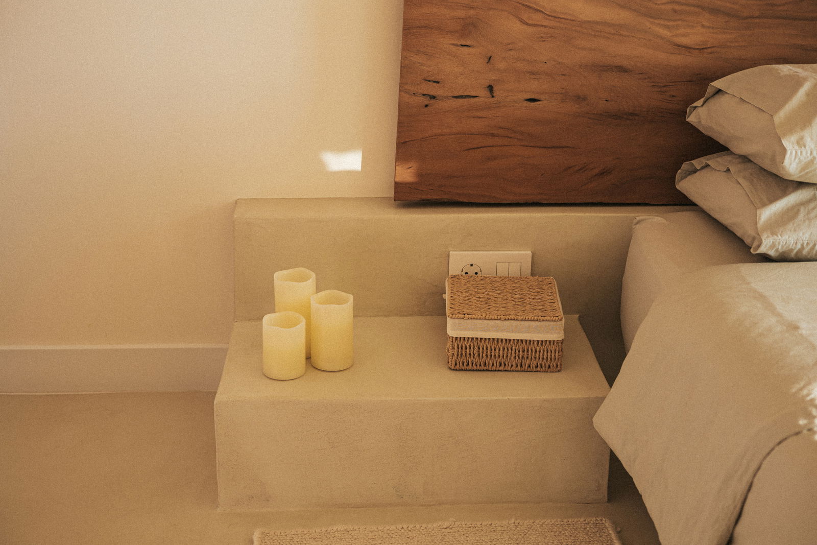 Drei cremefarbene Outdoor-Kerzen auf einem Treppenabsatz neben einem Bett, seitliche Perspektive.