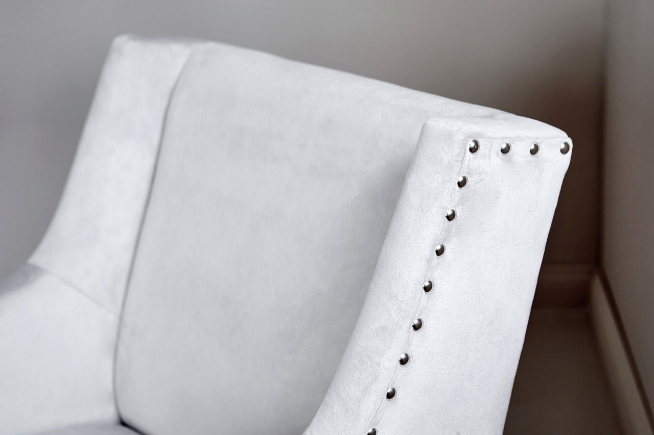 Nahaufnahme eines eleganten, hellgrauen Stuhls mit Nietenverzierung an der Lehne, seitliche Perspektive.