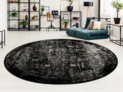 Runder Designer Teppich in Schwarz mit grauen Mustern in einem modernen Wohnzimmer, Perspektive von oben.