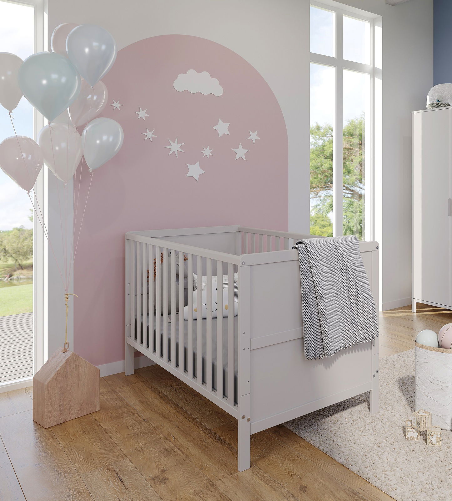 Babyzimmer mit weißem Gitterbett, rosa Wand mit Wolken- und Sternendekoration, Luftballons und großem Fenster, Perspektive von schräg vorne.
