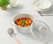 Ein Kochtopf mit Deckel, gefüllt mit einem Eintopf aus Gemüse und Wurst, auf einem Tisch mit weißem Tischtuch. Perspektive von oben.